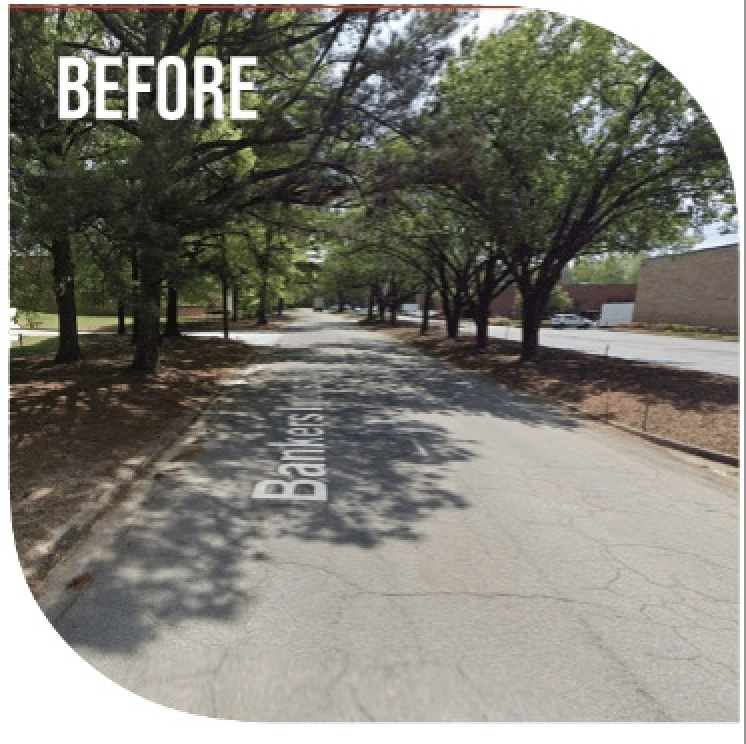 An empty road with sidewalks and grassy areas alongside it and a group of trees casting shade on the road in the background.