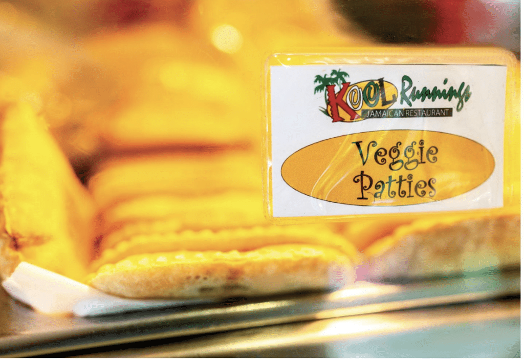 A tray of Jamaican fried veggie patties from Kool Runnings in Norcross, GA. There is a small sign with the Kool Runnings logo and Veggie Patties on the glass in front of the tray.