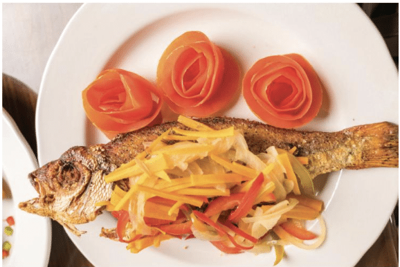 Cooked whole fish on a white plate with vegetables