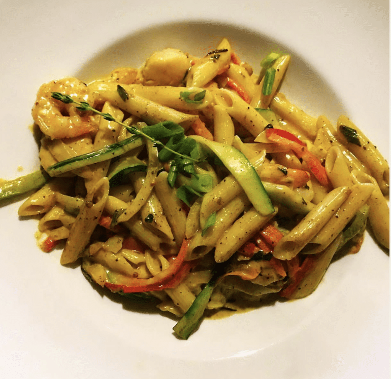 A plate of Rasta Pasta from Kool Runnings in Norcross, GA. Creamy pasta dish with vegetables and red peppers served on a white plate.