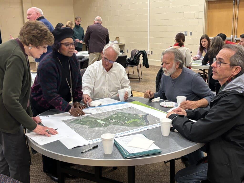 A group of people at a community meeting sitting around a table looking at proposed plans for Simpsonwood Park