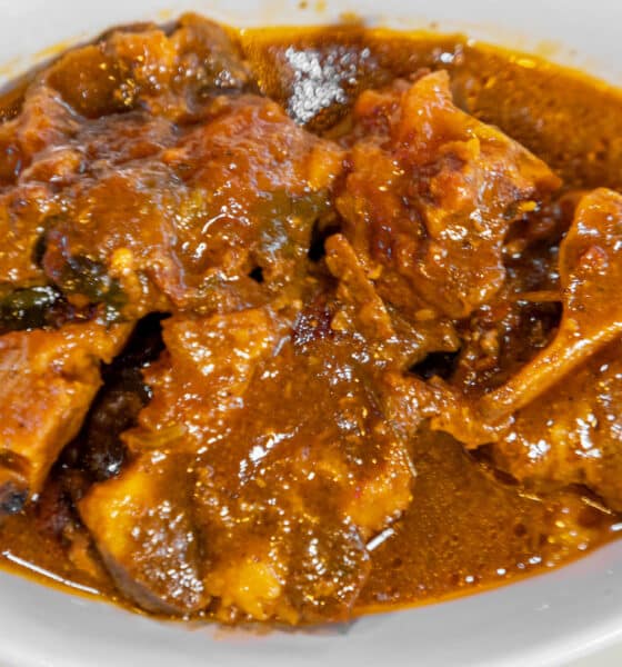 A plate of cooked ox tails in a brown sauce, served in a wide, white shallow bowl.