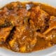 A plate of cooked ox tails in a brown sauce, served in a wide, white shallow bowl.