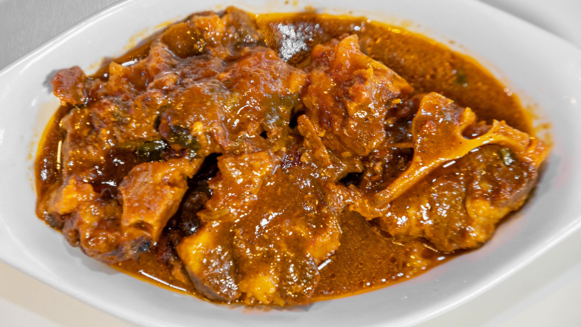 A plate of cooked ox tails in a brown sauce, served in a wide, white shallow bowl.