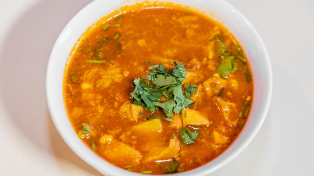 Dominican tripe soup in a white bowl with green herbs on top for garnish.