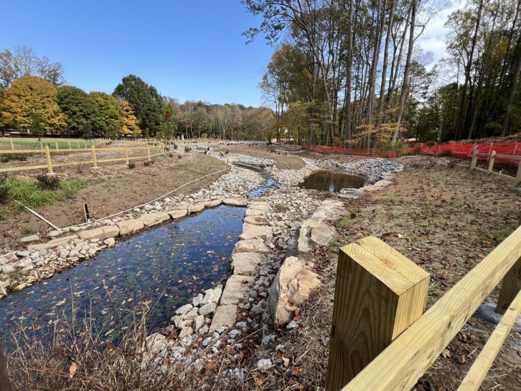 Park renovations with wooden fencing, small stream, fall trees and blue sky