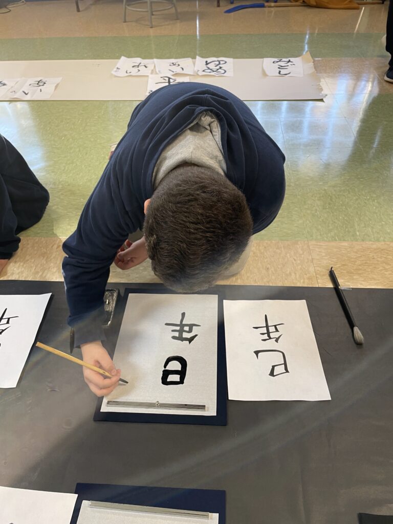 Student practicing Japanese calligraphy with brush and ink