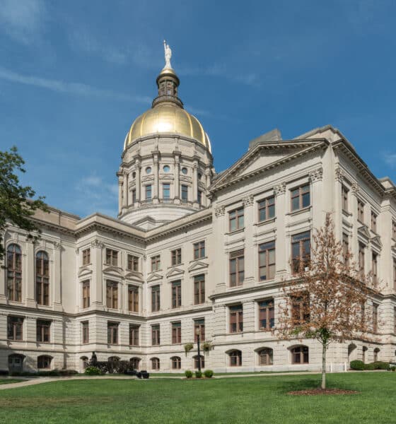 Georgia State Capitol building with green grass in front, trees on either side and blue sky overhead.