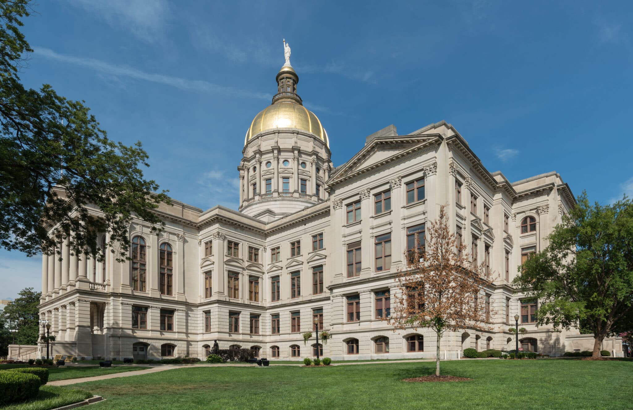 Georgia State Capitol building with green grass in front, trees on either side and blue sky overhead.