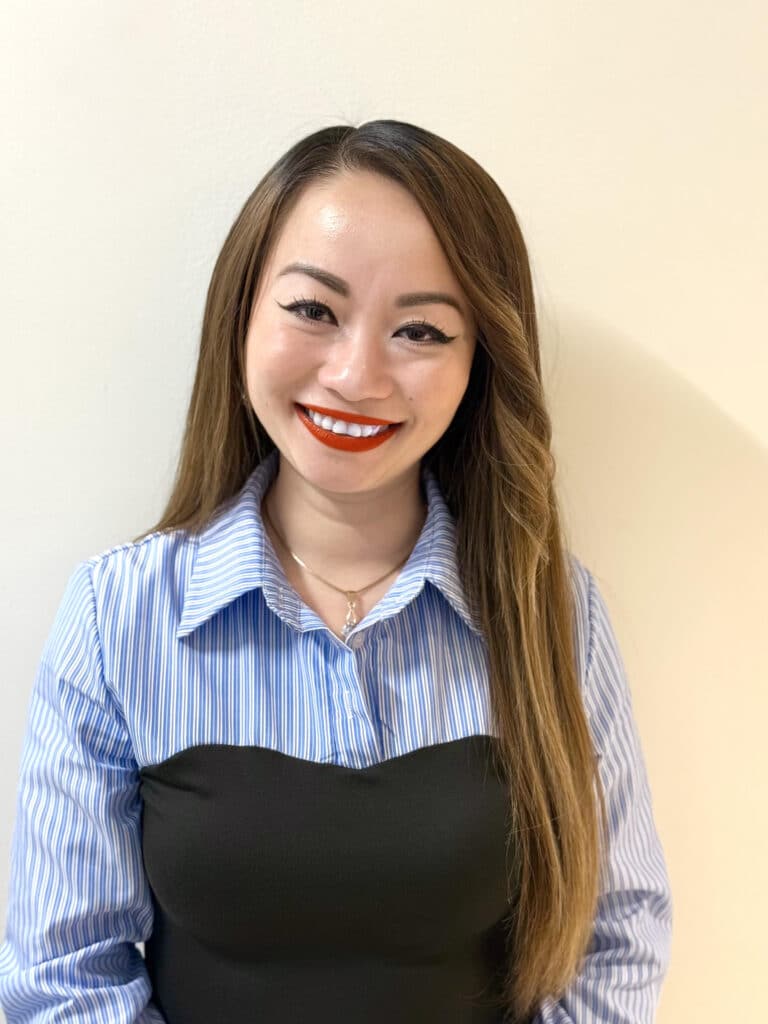 A young, smiling Asian woman with long hair and red lipstick. She's wearing a blue, collard blouse.