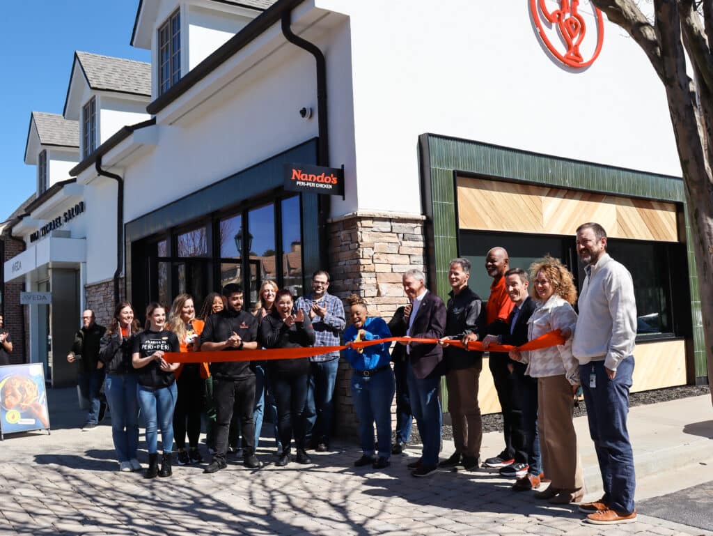 A group of people standing outside on a sunny day in February at a ribbon cutting ceremony for Nando's PERi-PERi at The Forum in Peachtree Corners