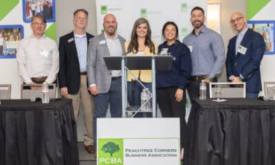 A group of people at a podium during a PCBA panel event. The organization's signage is in front of them and in the background.