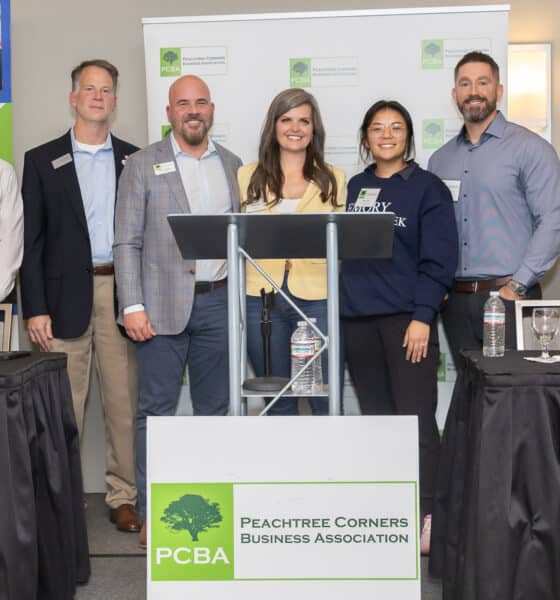 A group of people at a podium during a PCBA panel event. The organization's signage is in front of them and in the background.
