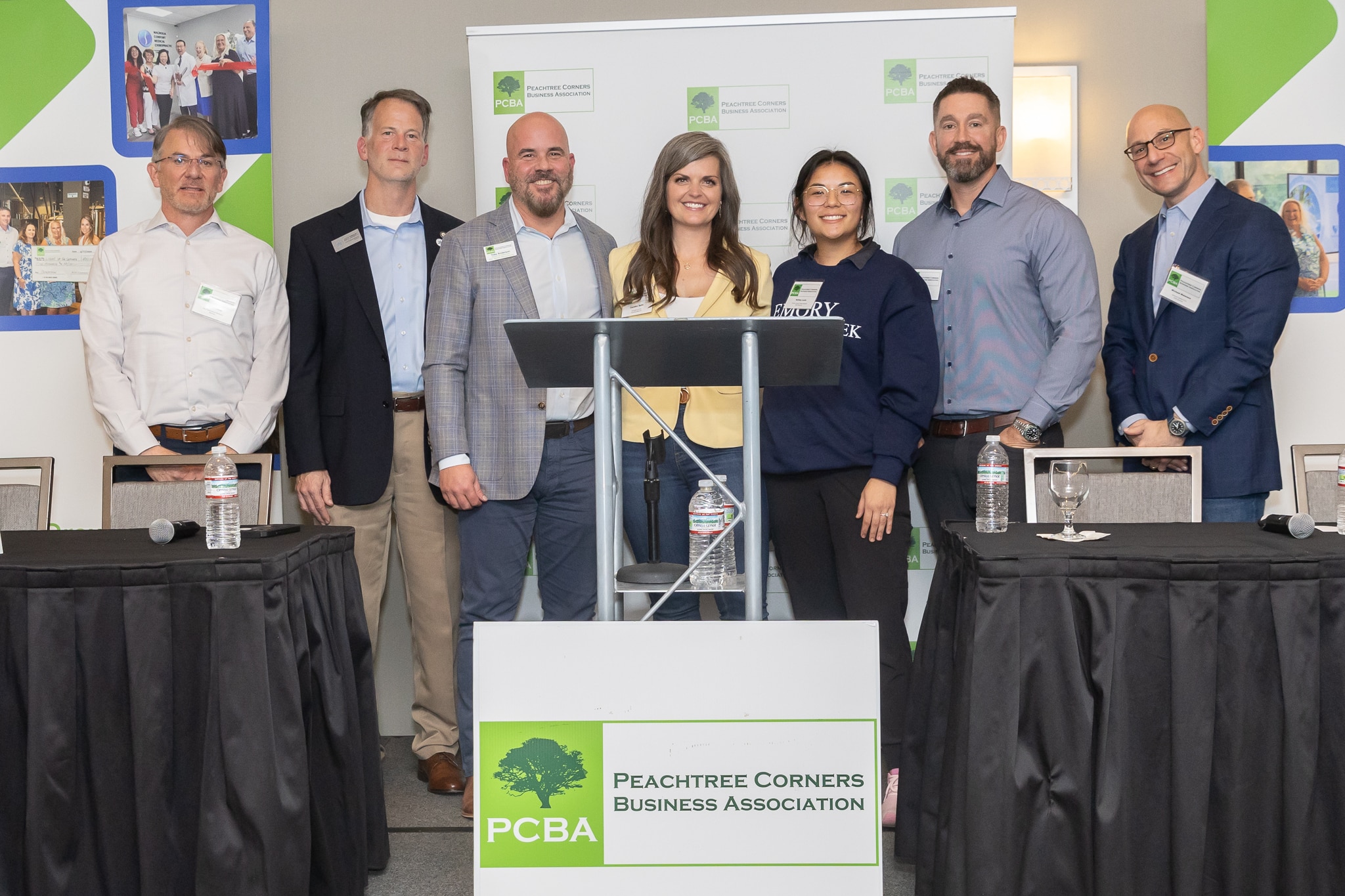 A group of people at a podium during a PCBA panel event. The organization's signage is in front of them and in the background.