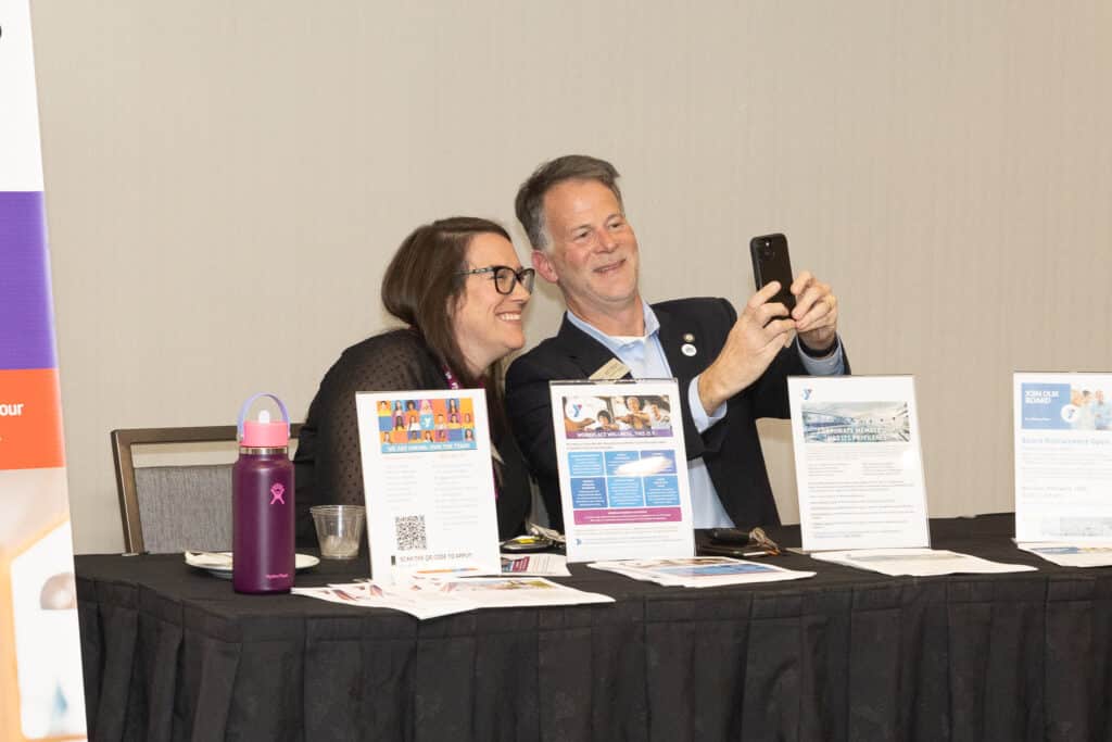 a man and a woman sitting at an event booth for the YMCA taking a selfie