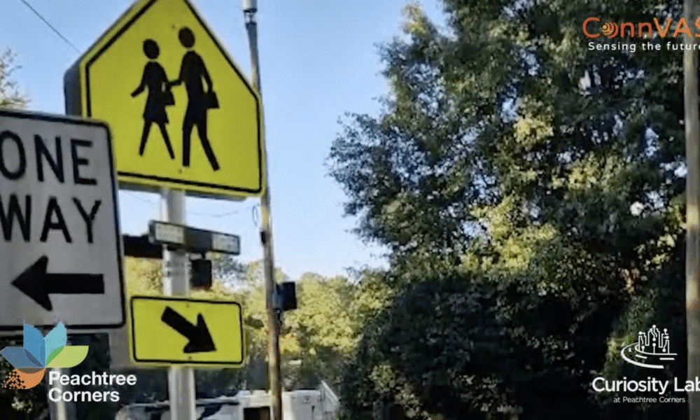 Pedestrian Crossing and One Way signs in a suburban neighborhood. There are power lines overhead and trees in the background.