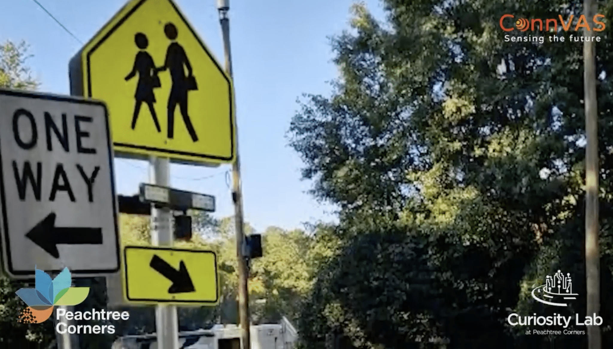 Pedestrian Crossing and One Way signs in a suburban neighborhood. There are power lines overhead and trees in the background.