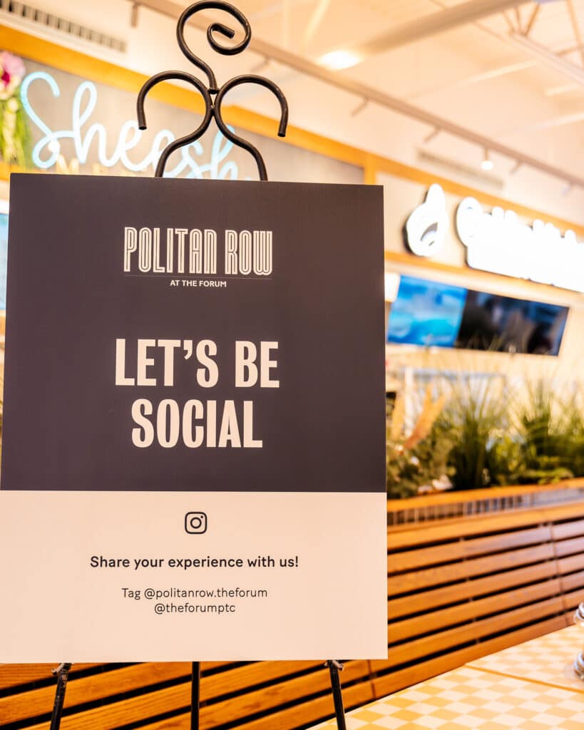 Signage from the Politan Row dining hall at The Forum which reads "Let's Be Social" and encourages diners to share photos of the space online and tag them.