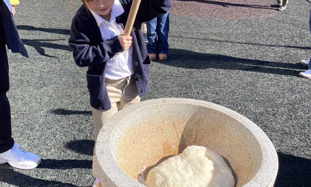 Young student pounding sticky rice with a large wooden mallet at an outdoor Japanese new year event