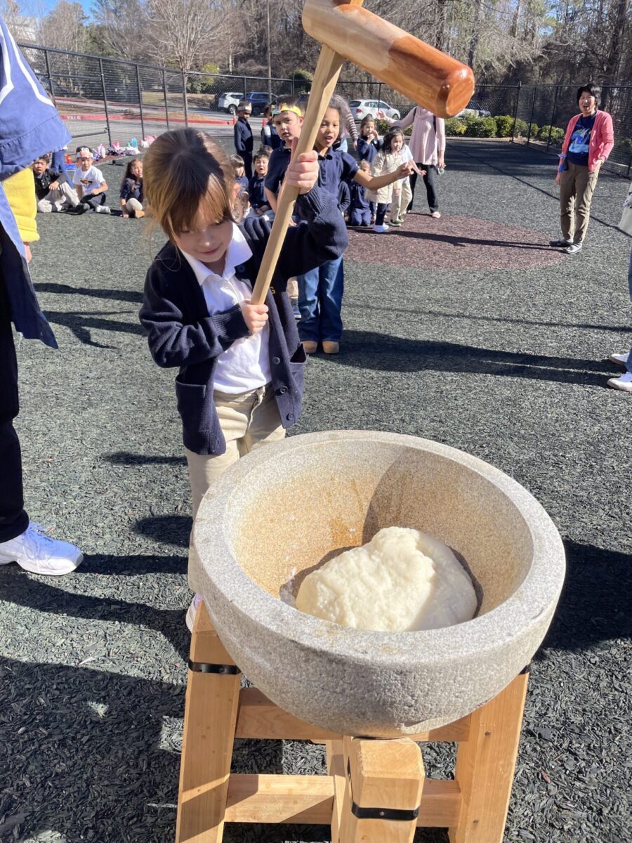 Young student pounding sticky rice with a large wooden mallet at an outdoor Japanese new year event