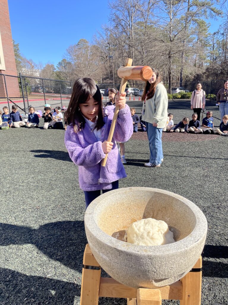 Student at a dual-language school pounding rice with a wooden mallet at Japanese new year event.