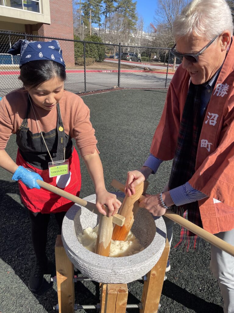 Volunteers at a dual-language school pounding rice with a wooden mallet at Japanese new year event.