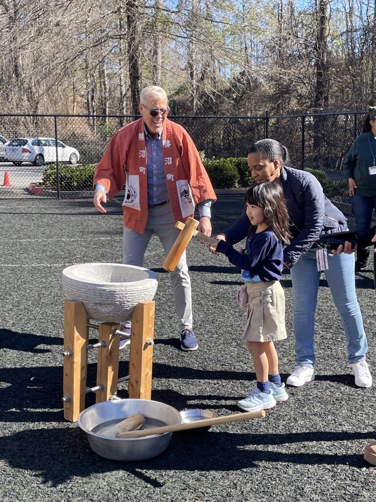 Student at a dual-language school pounding rice with a wooden mallet at Japanese new year event.