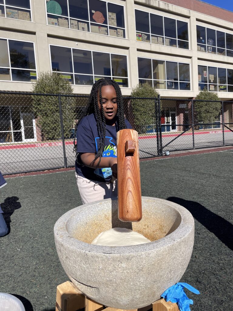 Student at a dual-language school pounding rice with a wooden mallet at Japanese new year event.