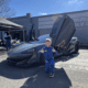 A smiling kid with blonde hair giving a thumbs up in front of an expensive sports car with it's driver door up.