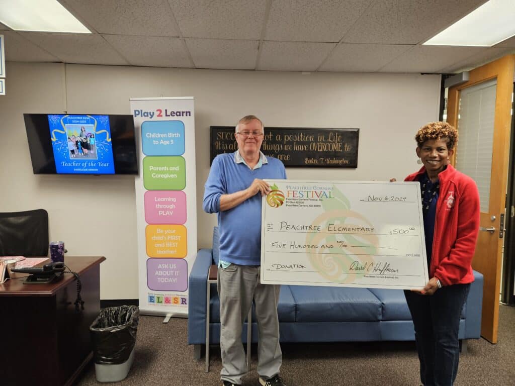 An older man in blue shirt holding a giant donation check with a representative of peachtree elementary school