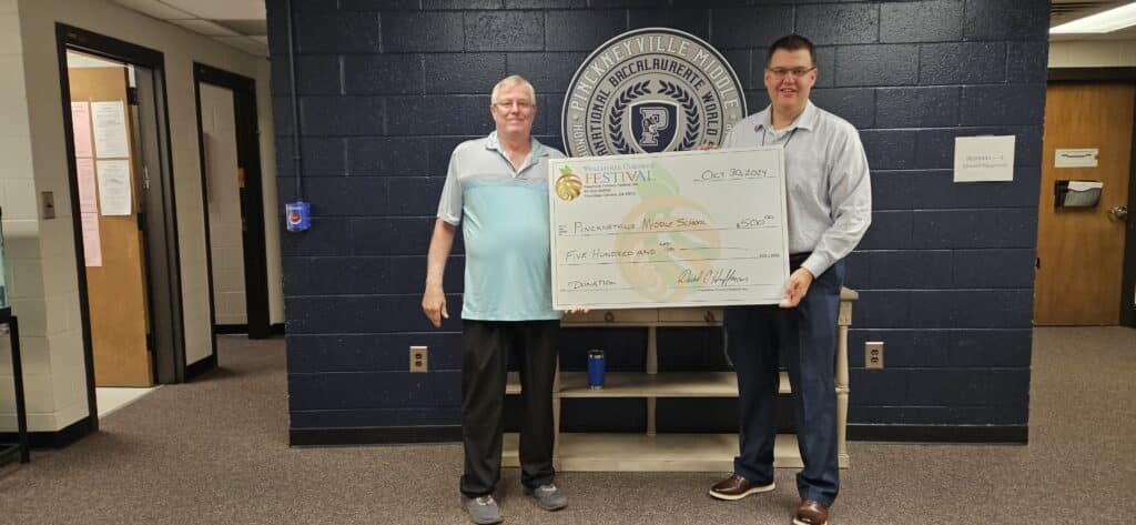 Two men holding a large donation check from Peachtree Corners Festival to Pinckeyville Middle School