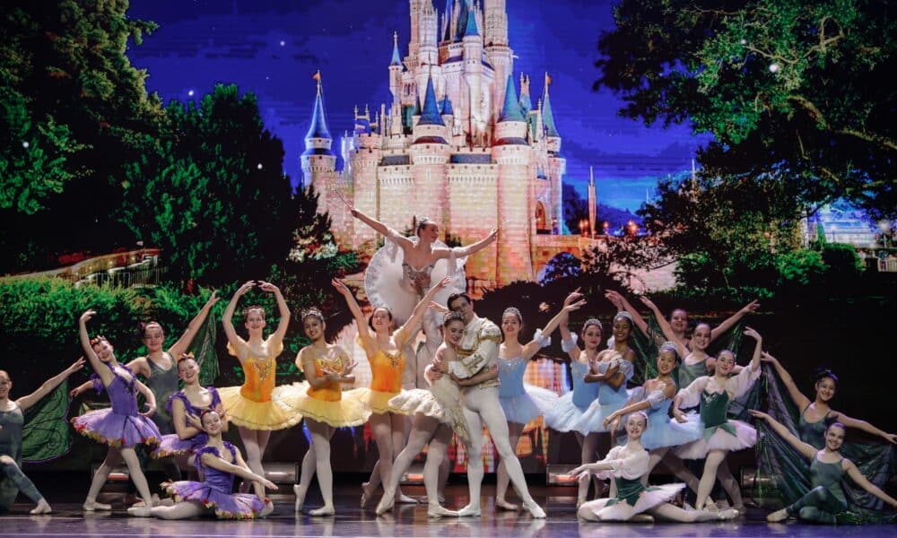 Ballet dancers on stage during a production of Cinderella. The dancers are posed in front of a lit backdrop of Cinderella's castle.