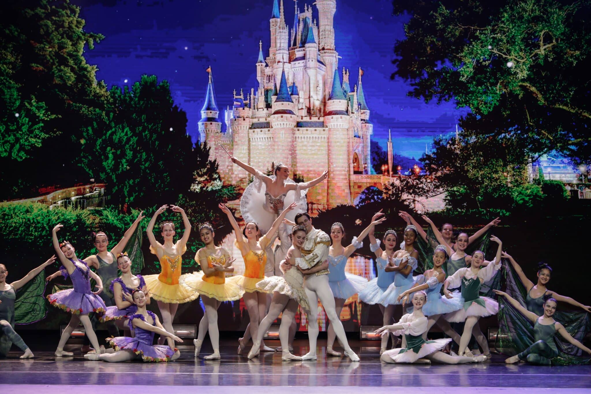 Ballet dancers on stage during a production of Cinderella. The dancers are posed in front of a lit backdrop of Cinderella's castle.