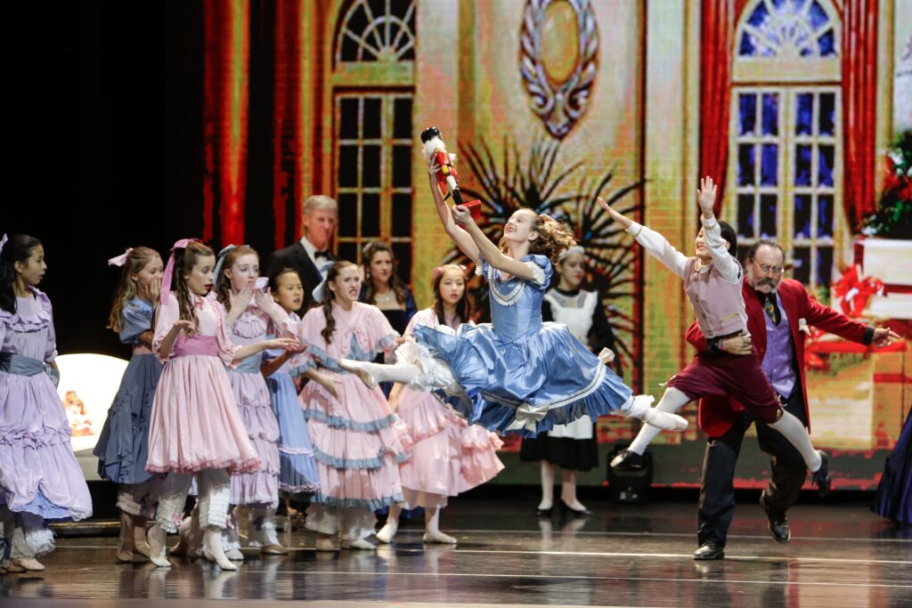 Ballet dancers on stage for The Nutcracker. Two dancers are leaping as the others stand around them in the background