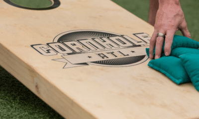 Close-up of a cornhole board and a hand reaching down to pick up blue/green beanbags.