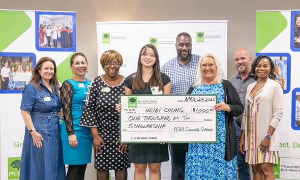 A group of people standing with a young Asian American high school senior. They are holding a large cardboard check made out for $1,000 as a scholarship for the teen.