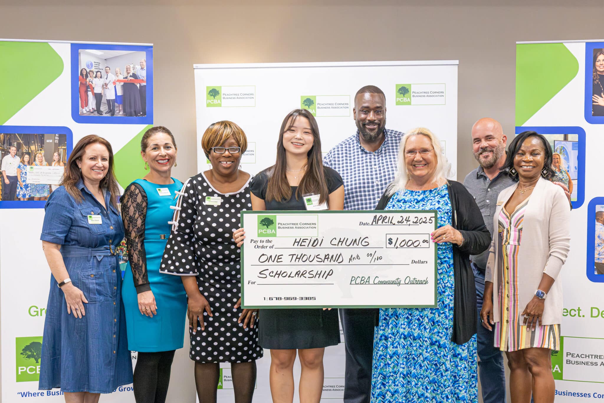 A group of people standing with a young Asian American high school senior. They are holding a large cardboard check made out for $1,000 as a scholarship for the teen.