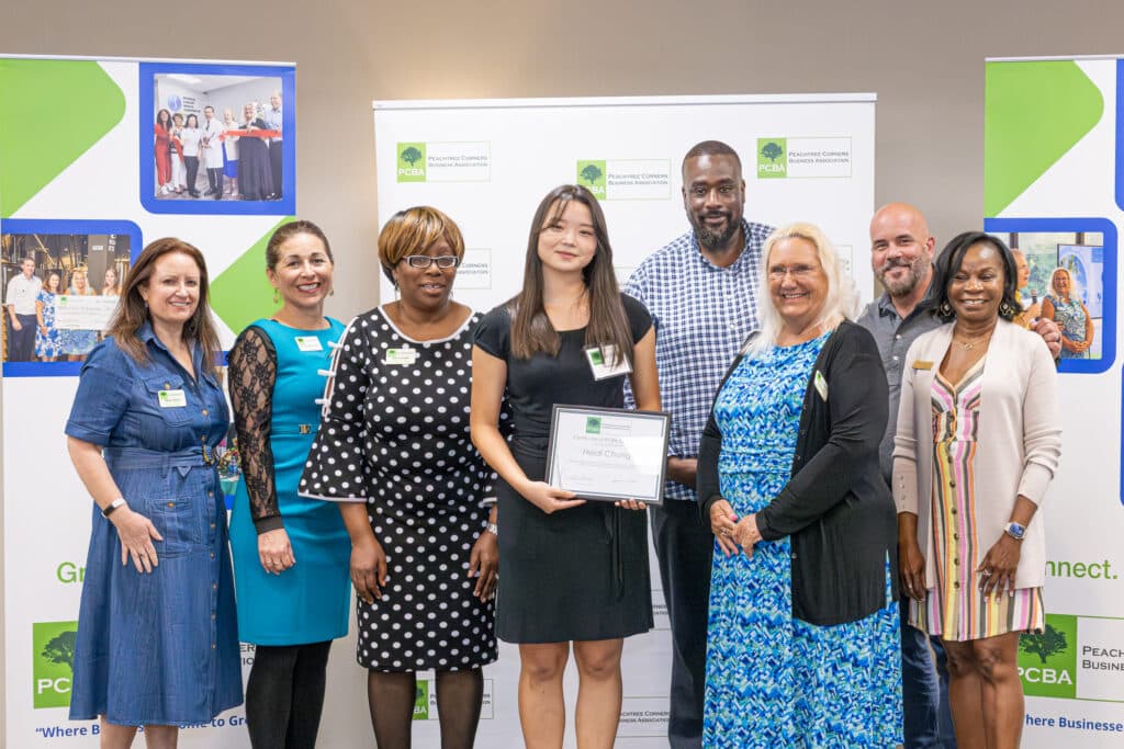 A group of people from the PCBA standing with a young Asian American, female high school senior. They are presenting her with a scholarship for $1,000.