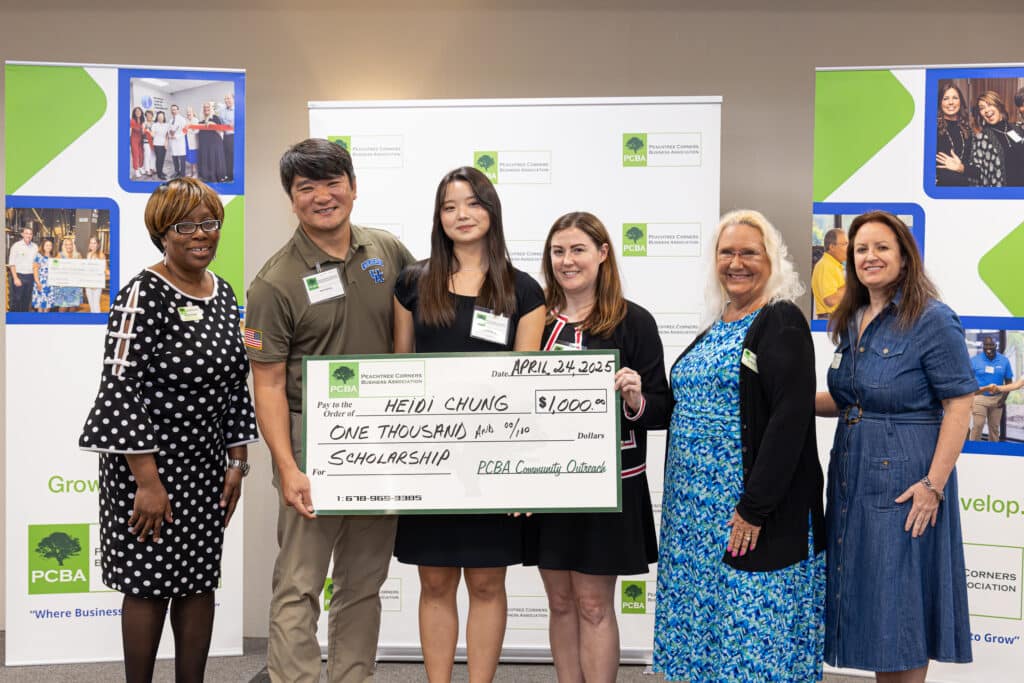 A group of women from the PCBA standing with an Asian American high school girl and her parents. They are holding a large cardboard check made out for $1,000 for a scholarship for the teen.