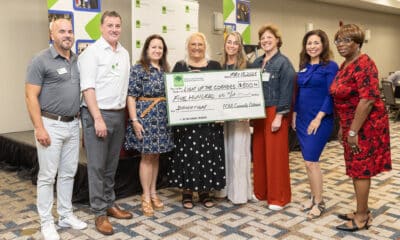 A group of people standing together at a business event, holding a large check made out for $500 to Light Up the Corners