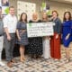 A group of people standing together at a business event, holding a large check made out for $500 to Light Up the Corners