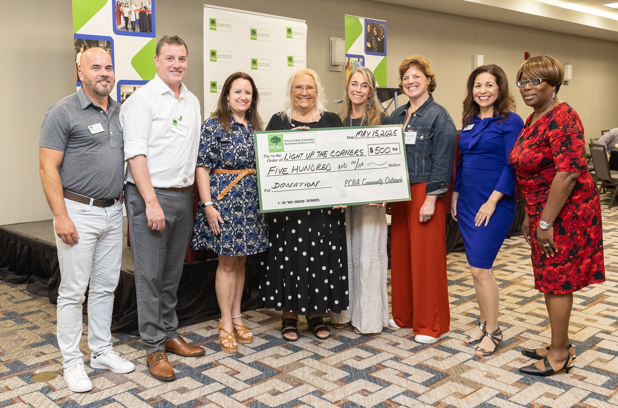 A group of people standing together at a business event, holding a large check made out for $500 to Light Up the Corners