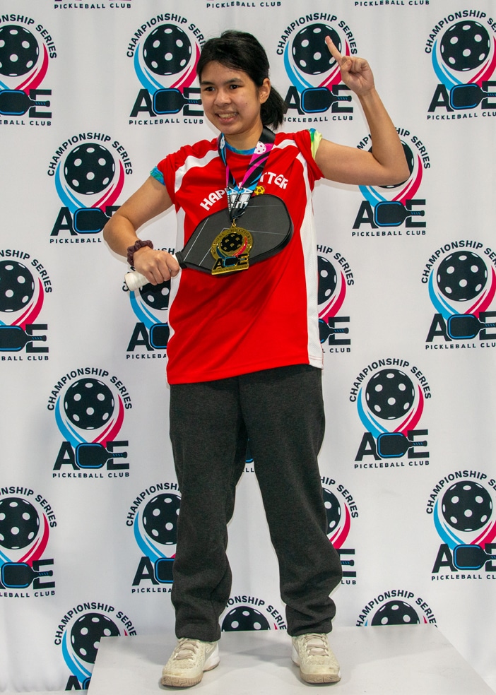 A female Special Olympics Pickleball athlete in her team uniform, wearing her medal and holding her paddle.