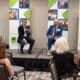 Two men sitting on chairs on a stage. They are holding microphones and answering questions from the audience at a business event