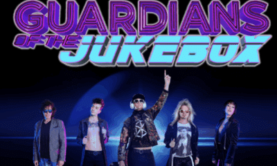 Guardians of the Jukebox 80s cover band in costume on stage with their 80s-style logo above them.