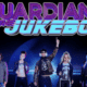 Guardians of the Jukebox 80s cover band in costume on stage with their 80s-style logo above them.