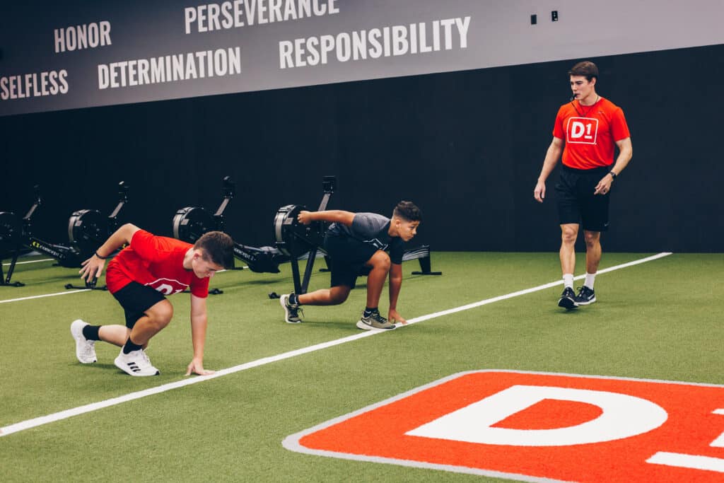 Young teen athletes in a runners starting position on an indoor field at a fitness facility.