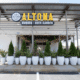 Front entrance of Altona Burger & Beer Garden in Norcross, Georgia. The building is white and modern. There's a row of green plants in white pots lining the entrance, separating it from the parking lot.