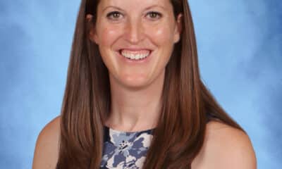 A white woman with long, straight brown hair. She's looking at the camera and smiling, wearing a sleeveless top, against a light blue background.