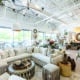 Interior of an upscale home design store with an L-shaped sofa, tables, other furniture and decor all in shades of cream and white.